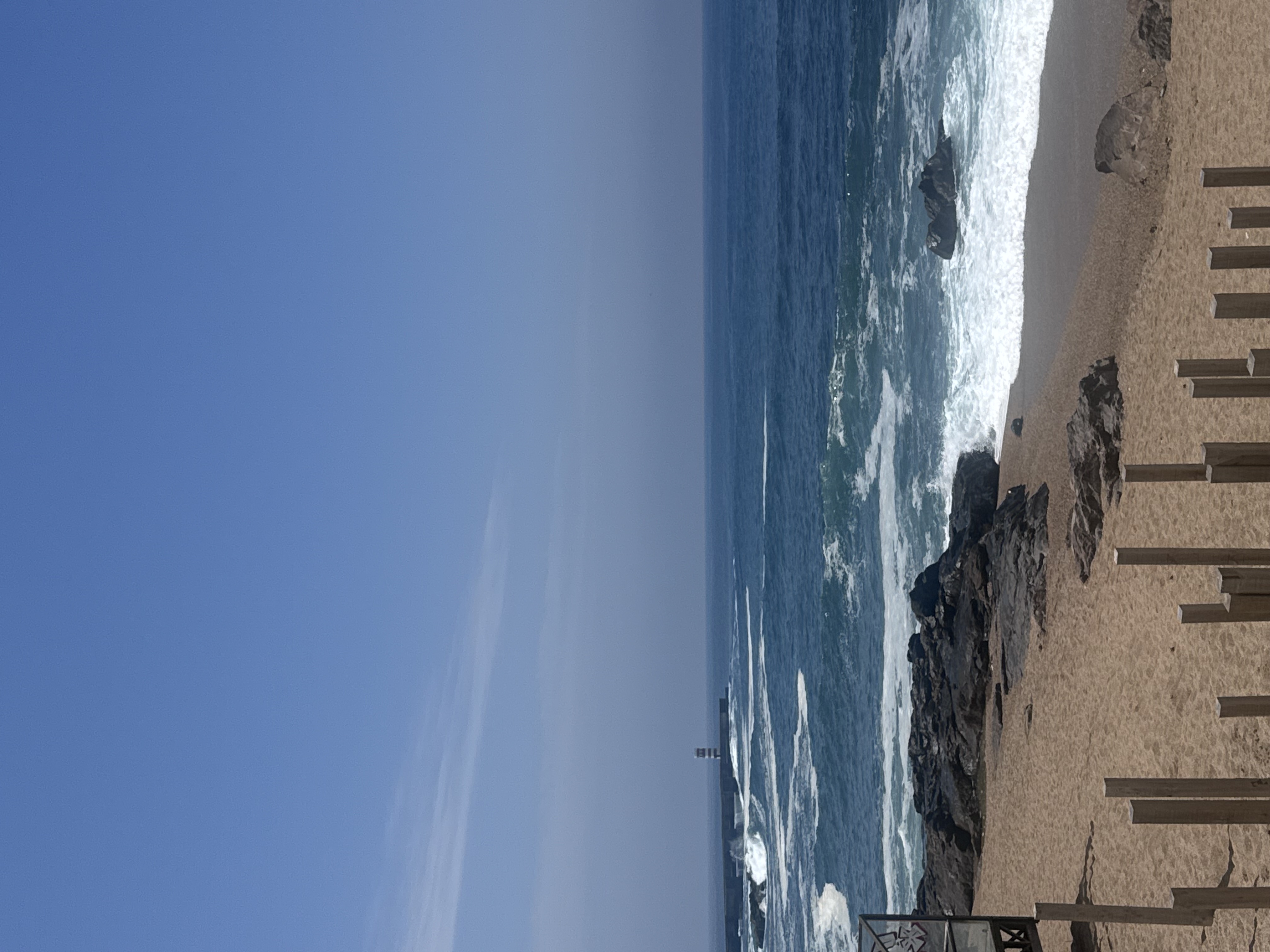 Steinerne Treppen führen hinab zum Meer. Das Wasser leuchtet blau, der Himmel ist klar. Links eine massive Mauer aus Sand- oder Naturstein mit breiten Treppenstufen. Das Licht ist scharf und deutlich.